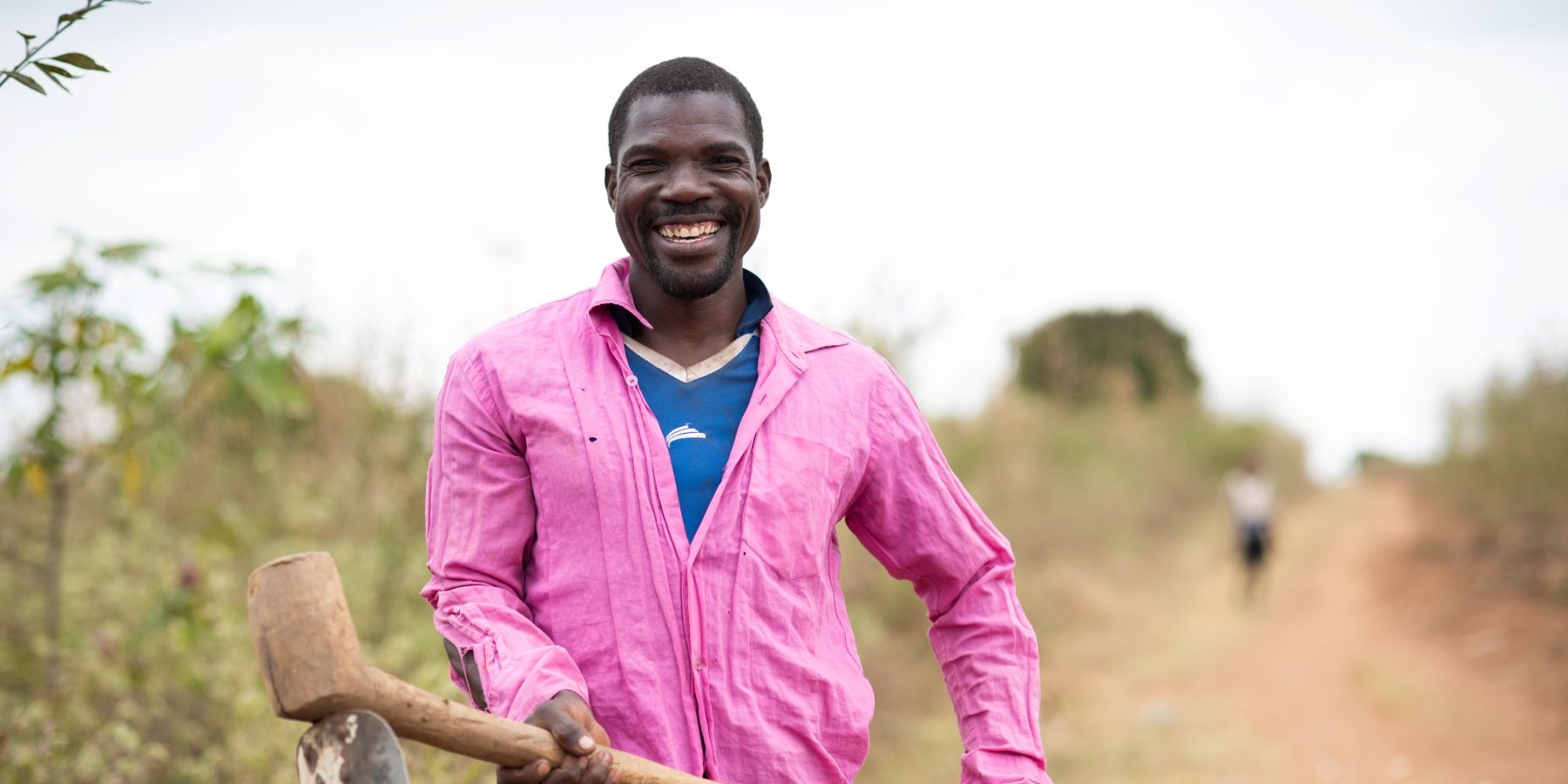 Handson John, a farmer in Malawi smiles at the camera as he holds his jembe