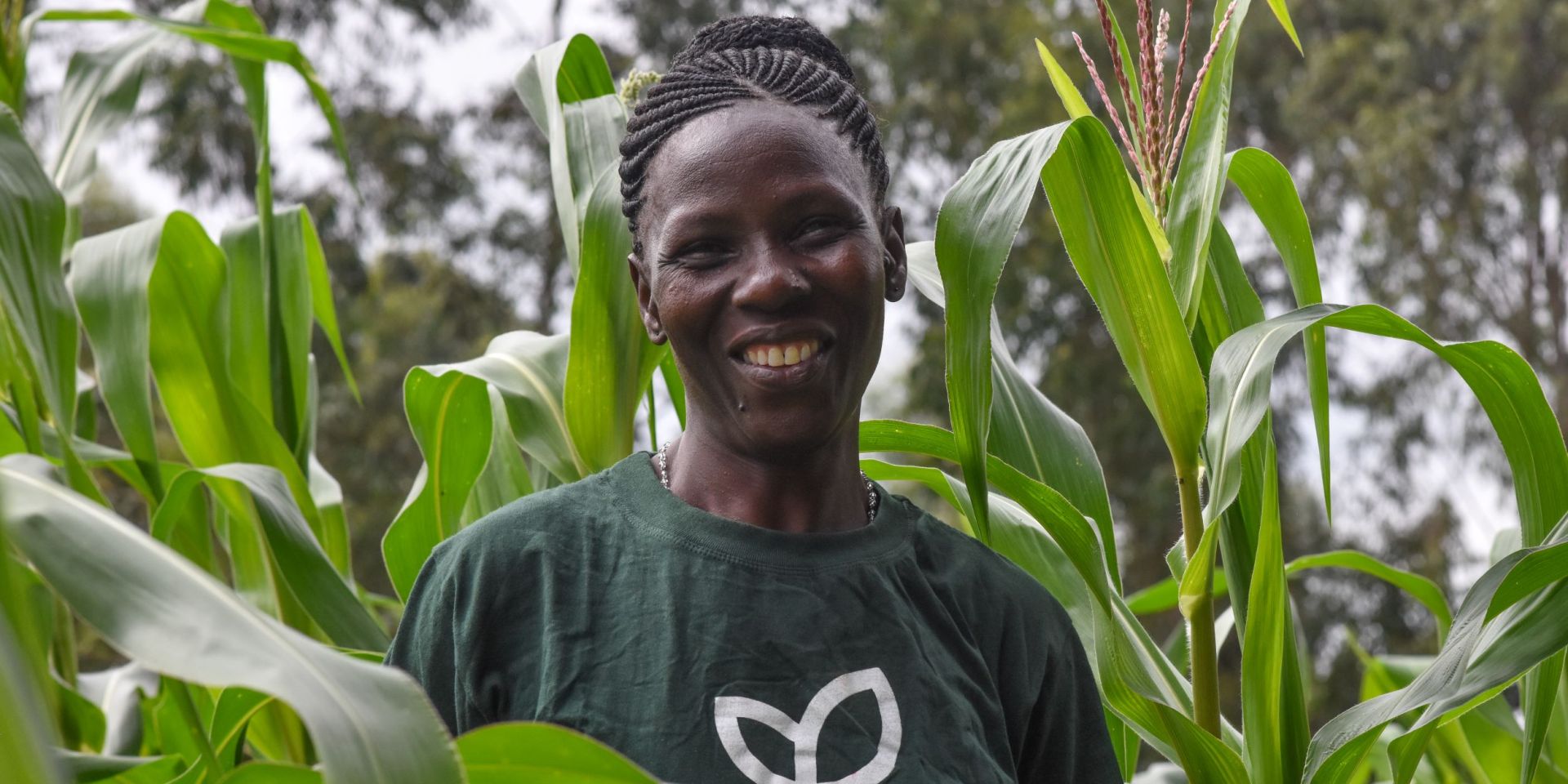 A smiling woman farmer stands in her field of maize