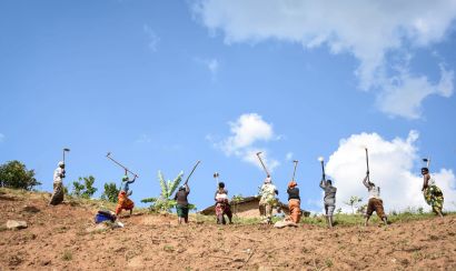 Farmers in Rwanda stand in a line tilling the soil