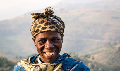 A farmer in Rwanda smiles at the camera as she stands in her field