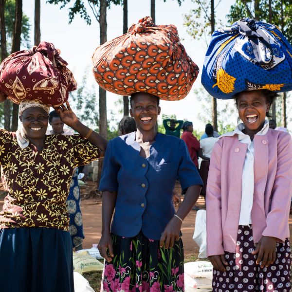 Three women stand with their bundles of farm supplies on their heads