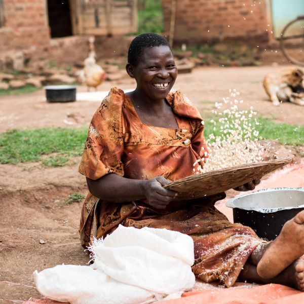 A farmer sits winnowing her maize at her home in Uganda