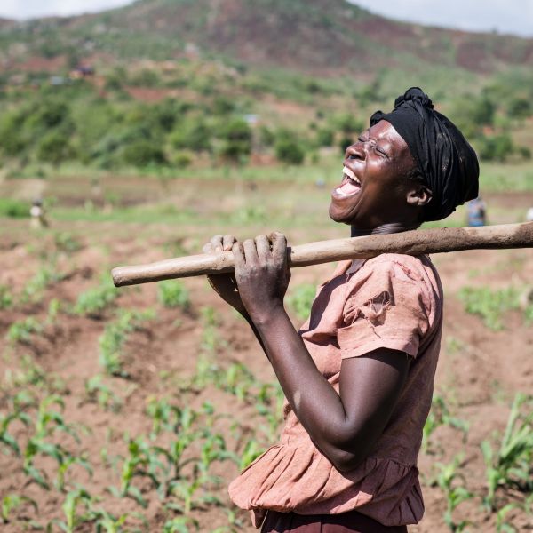 A female farmer laughing in her field with her jembe over her shoulder
