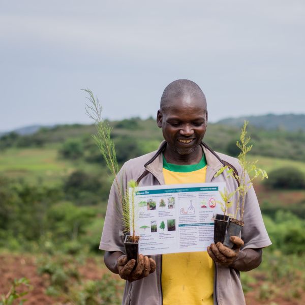 A farmer in Tanzania holds a planting card and some tree seedlings