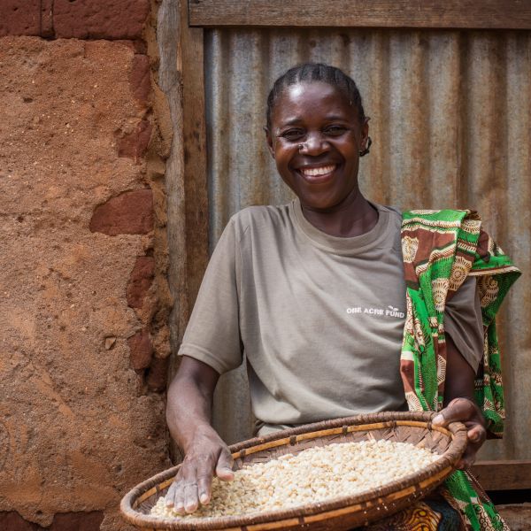 A female farmer in Tanzania smiles at the camera holding her maize basket