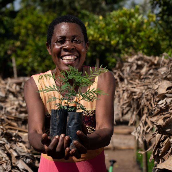 smiling woman holding up two tree seedlings 