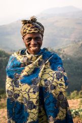 A farmer in Rwanda smiles at the camera as she stands in her field