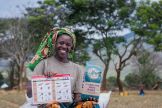 A farmer in Kenya shows off her farm inputs following an input delivery