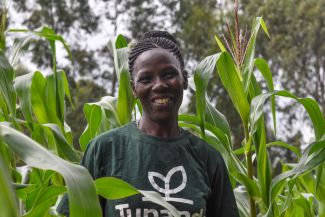 A smiling woman farmer stands in her field of maize