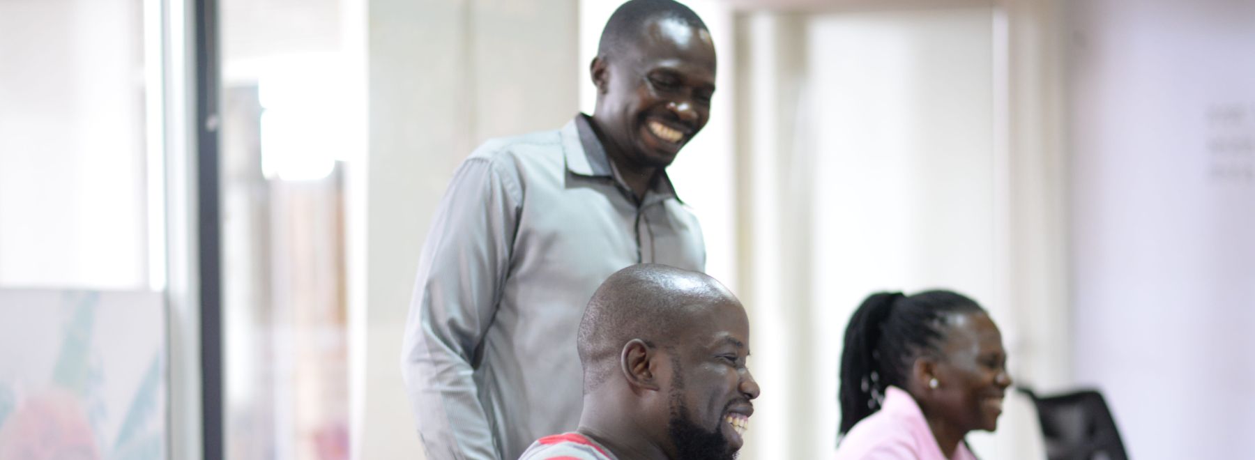 One Acre Fund team members in Uganda laugh together over a laptop screen