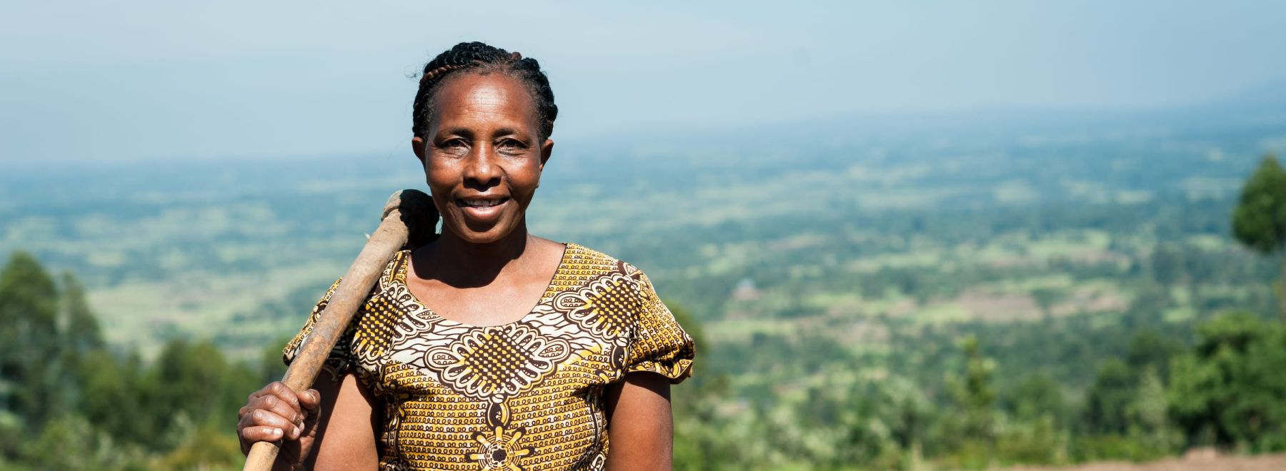 A female farmer stands in her field overlooking a beautiful view in Kenya