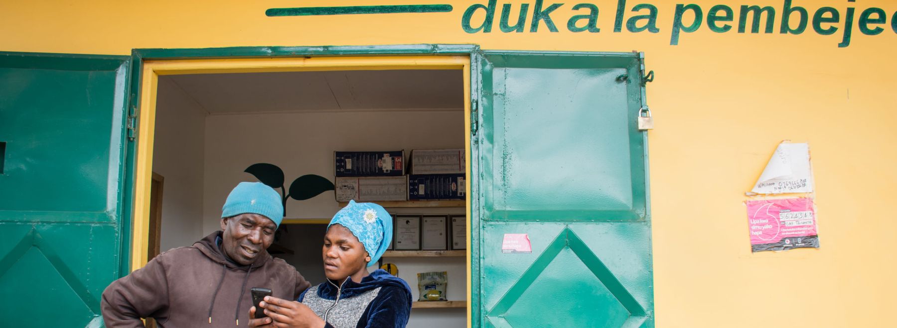 A One Acre Fund duka manager helps a customer outside a duka in Tanzania
