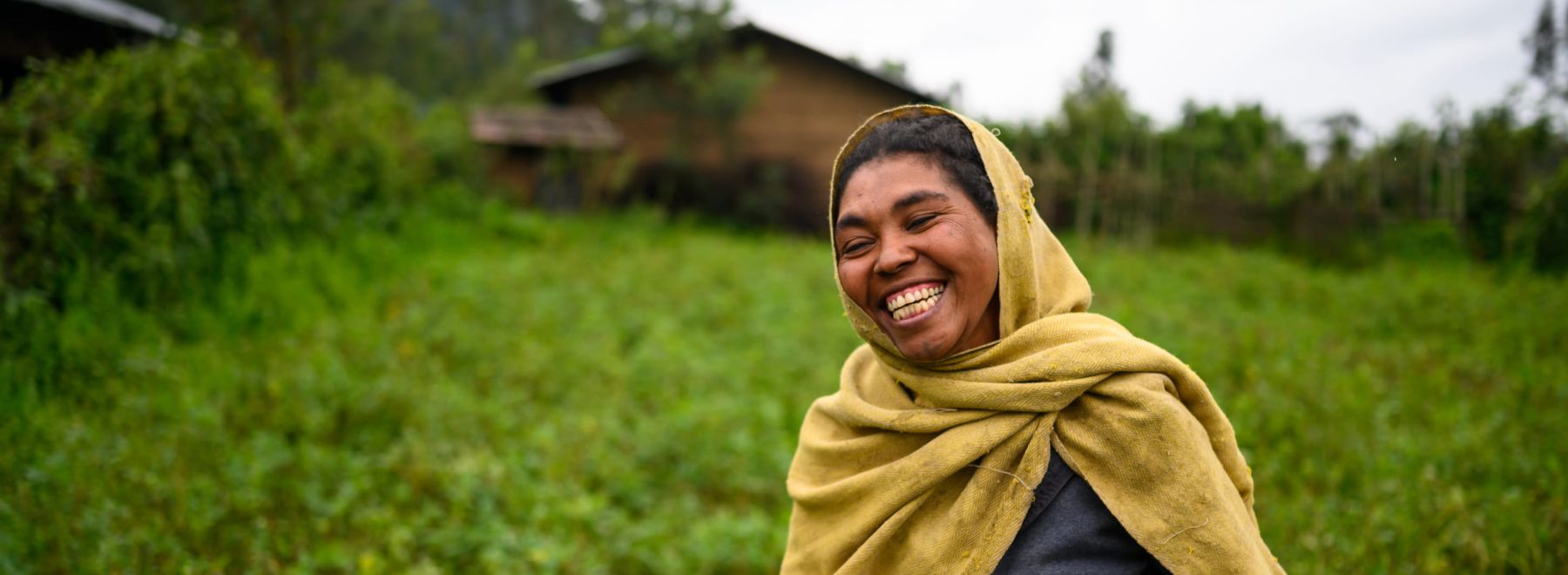 A farmer in Ethiopia laughs as she poses for a photo in front of her new tree seedlings
