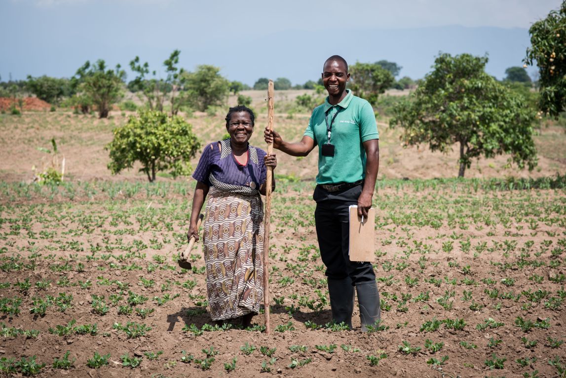 A farmer stands with her field officer in her field in Malawi