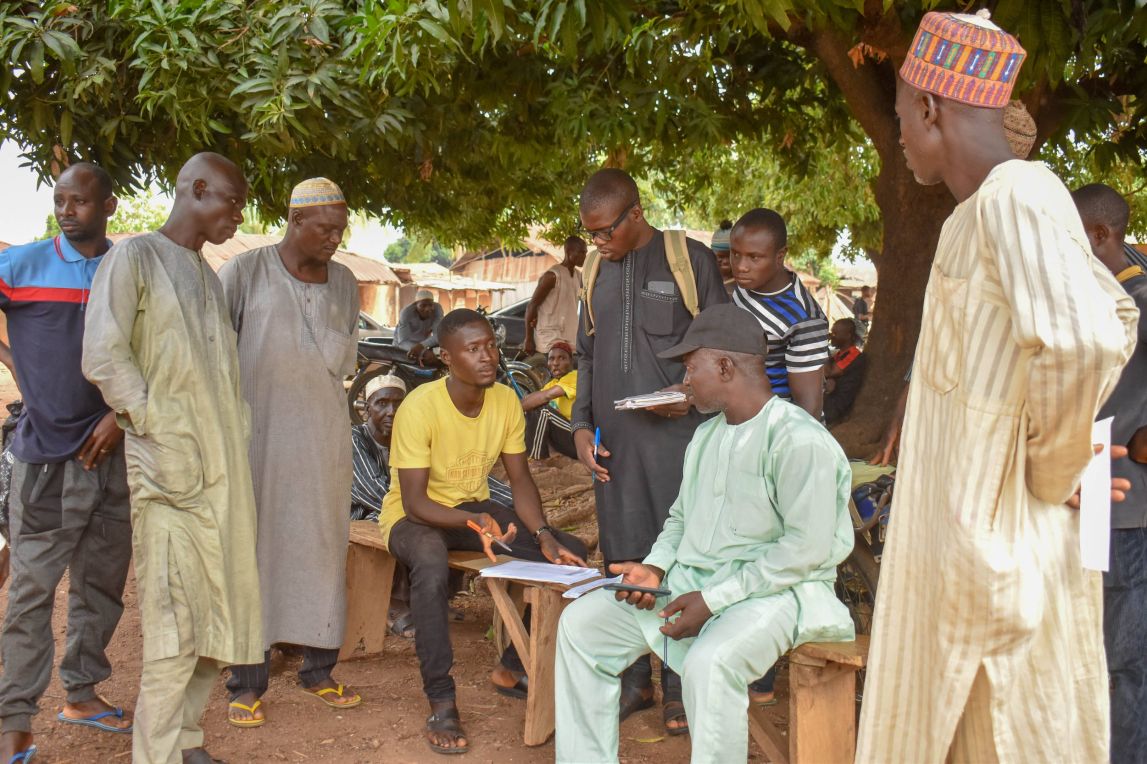 A group of mail farmers gathered around a man checking a document