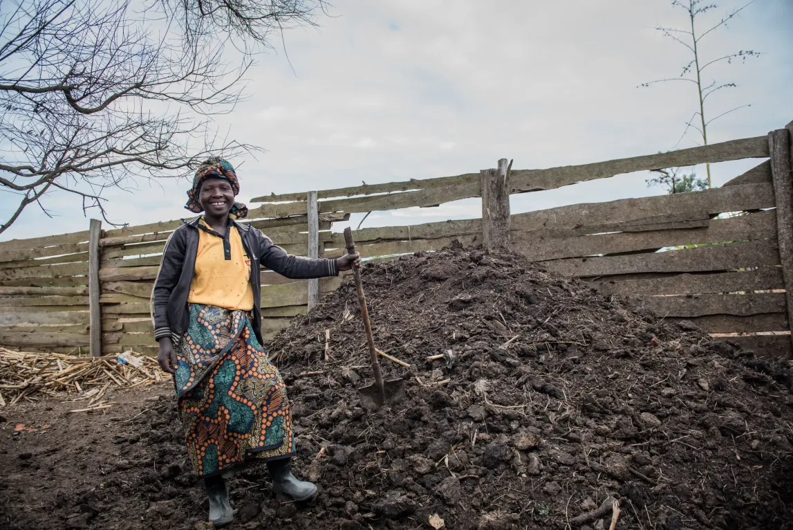 A smiling farmer stands in front of a mound of soil