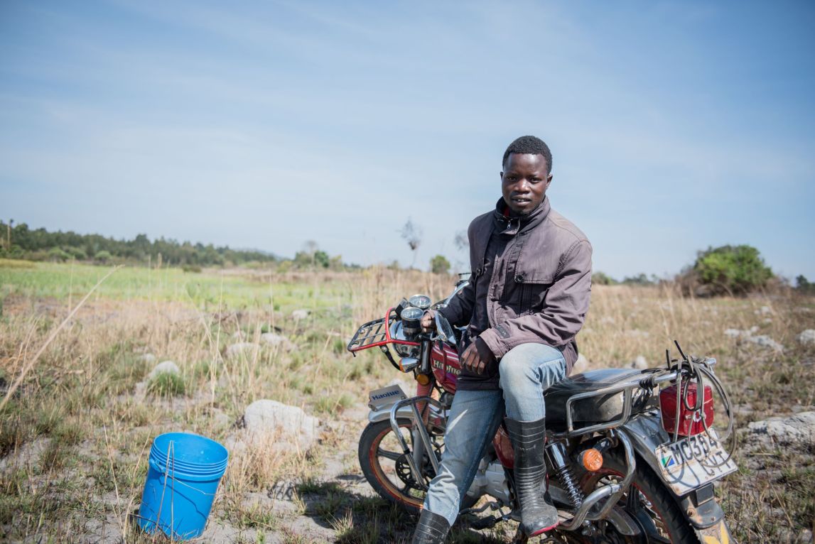 young person sitting on his motorbike in the middle of a field. 